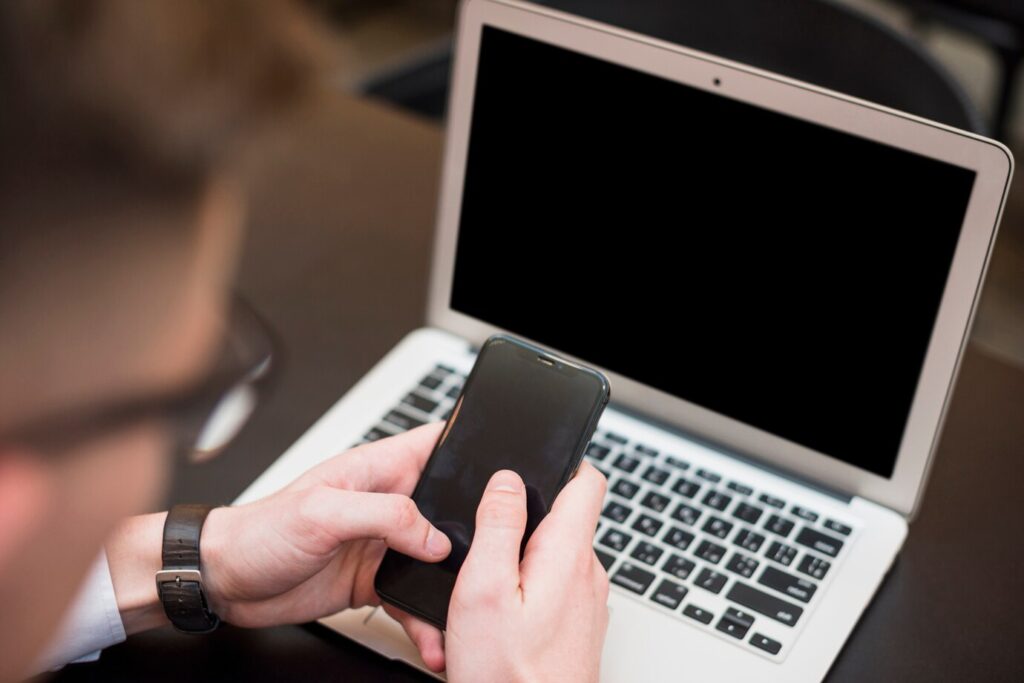 mao de um homem de negocios usando o celular na frente do laptop 23 2148096499